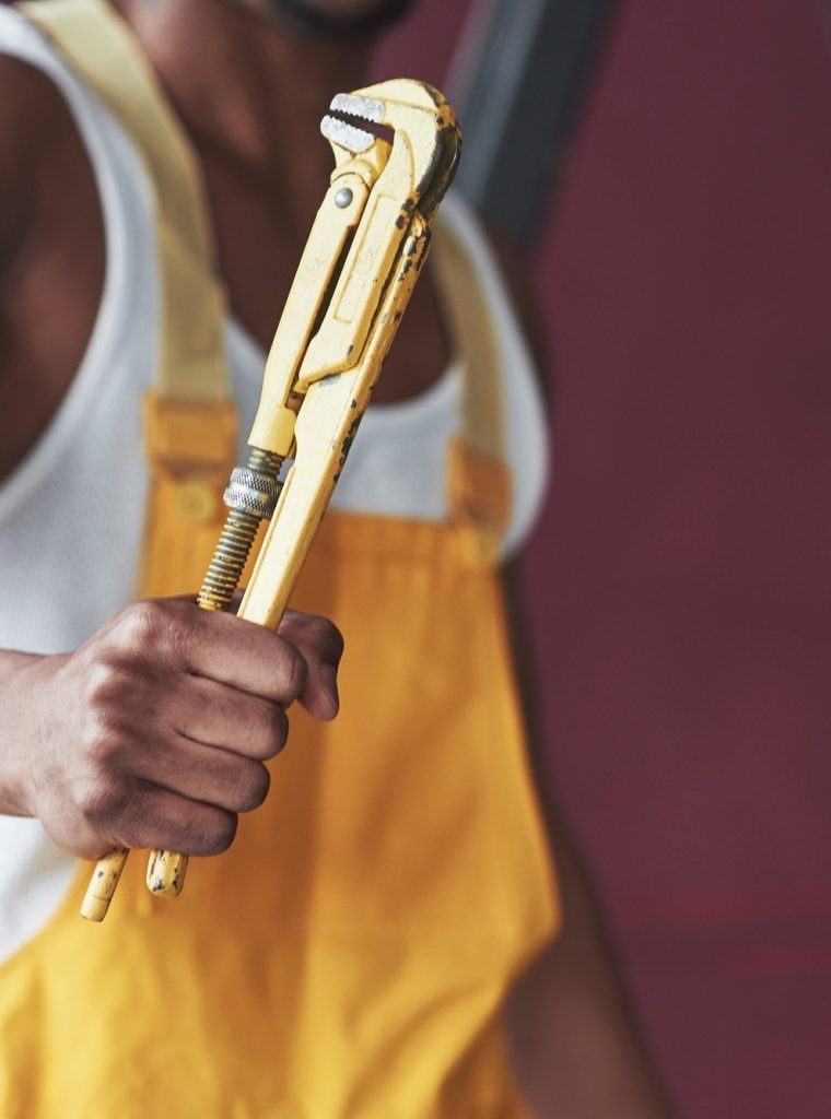 Yellow wrench in focus of camera. Young african american worker in the yellow uniform have some job